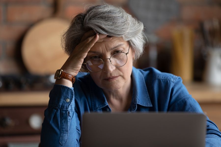 A white-haired woman looks at her computer with concern as she realizes her important online data was breached.
