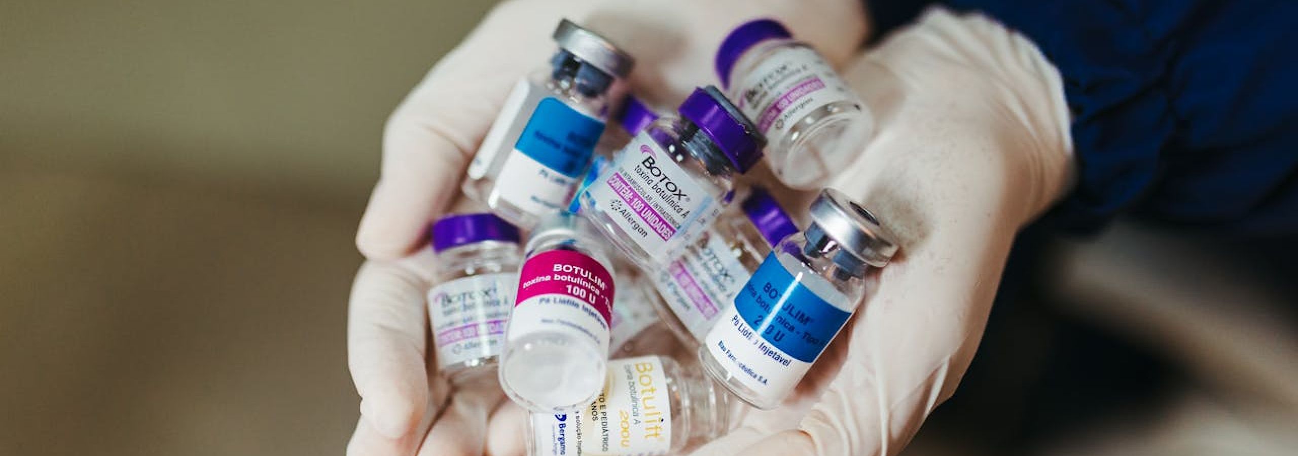 A healthcare worker with rubber gloves holding several empty botox containers.