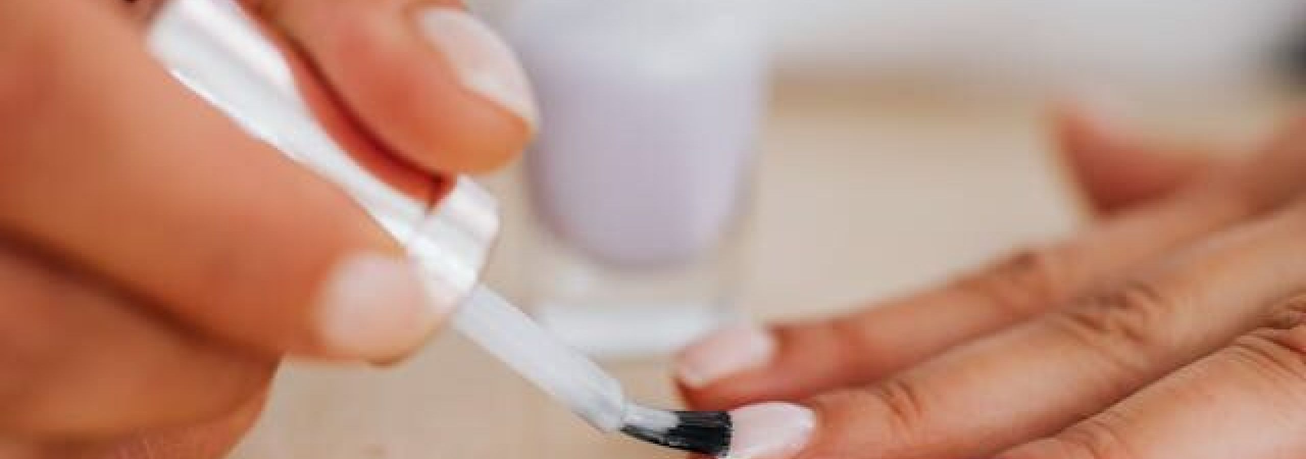 A woman applying white mail polish to her fingernails