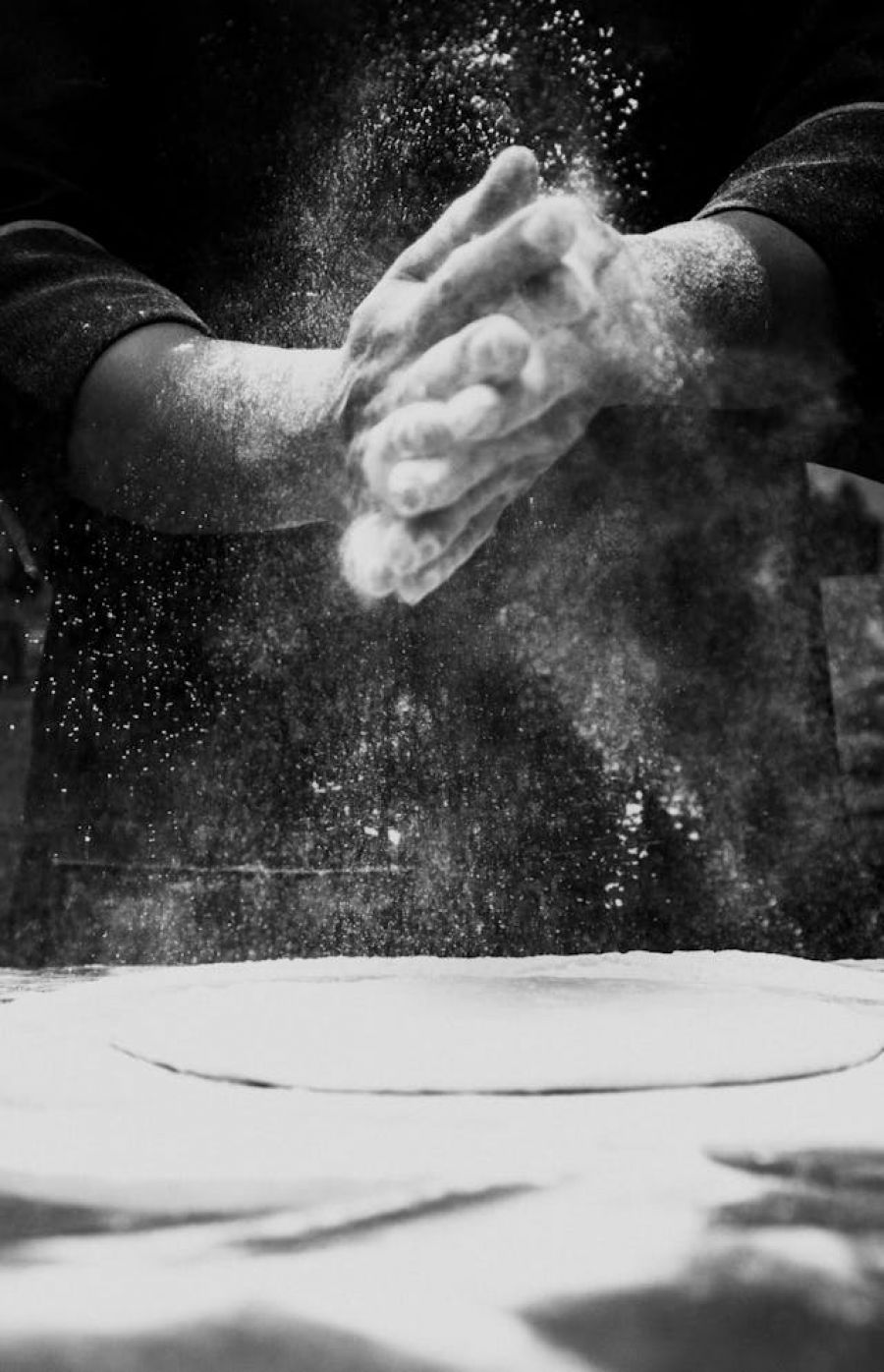 A man kneading dough in preparation of rolling our a pizza base.
