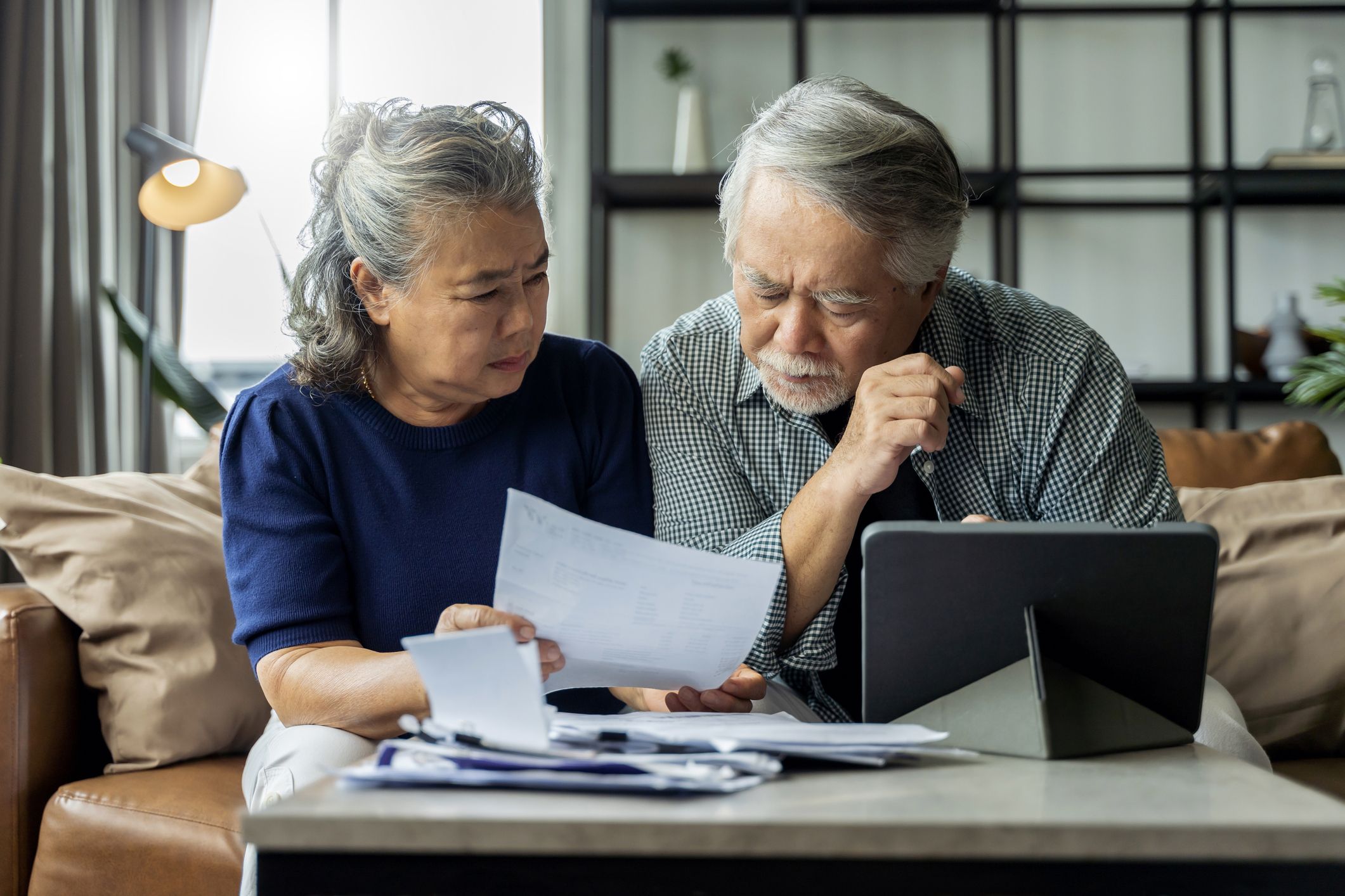 A white-haired Asian couple compare their bills to a computer tablet and realize their data has been stolen.