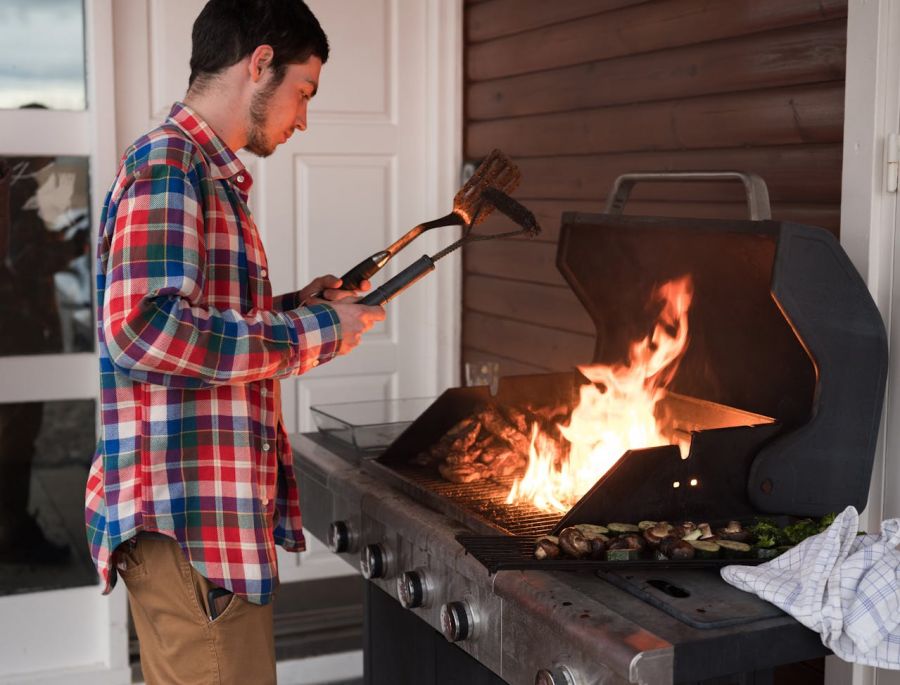 a man is standing over a grill with a spatula and a grill brush