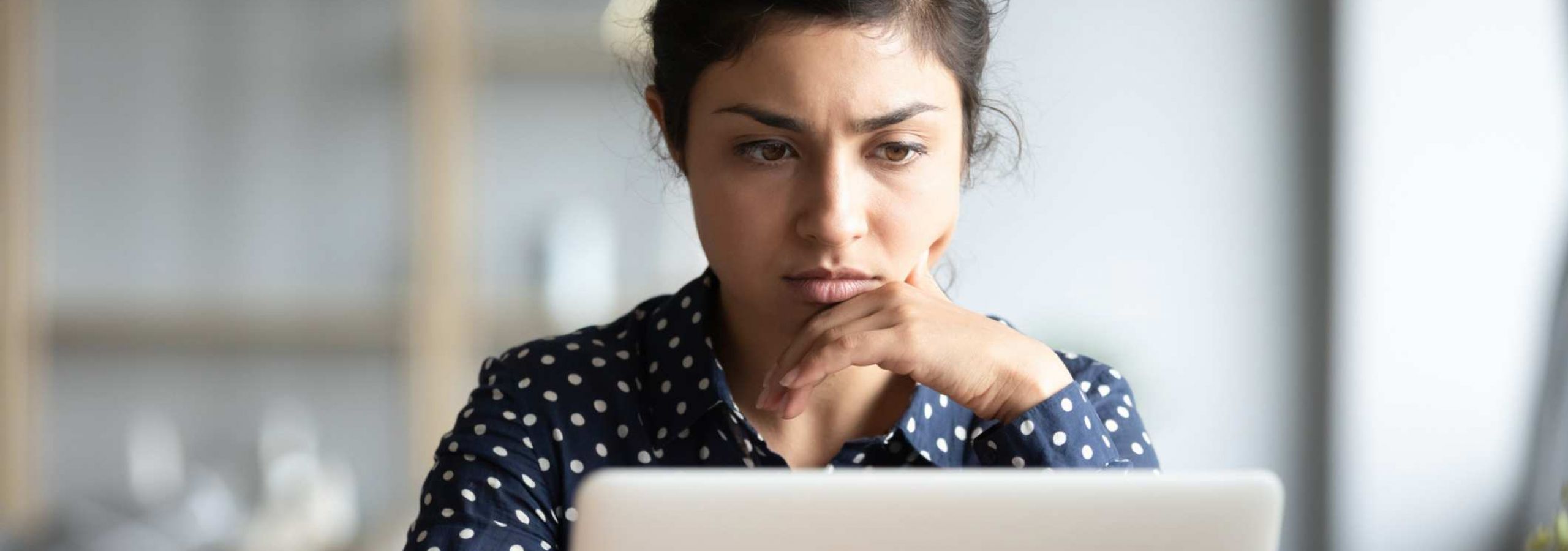 A woman concernedly looks at her laptop screen, fearing that she has been a victim of data misuse.
