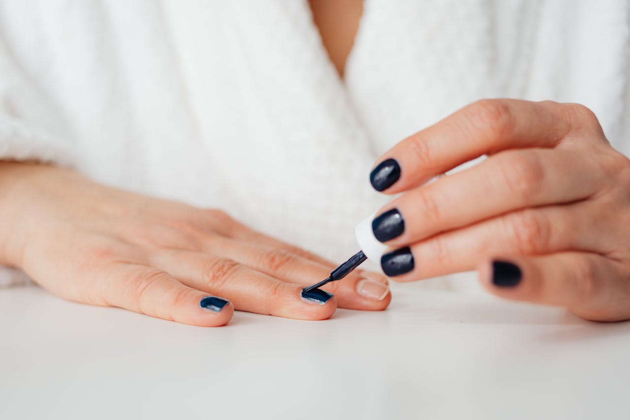 A woman in a white robe applying nail polish to her fingers