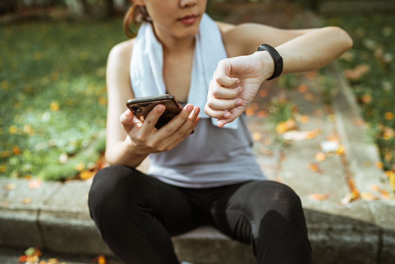 A woman checking her wearable device and her phone for the health data it collects and stores