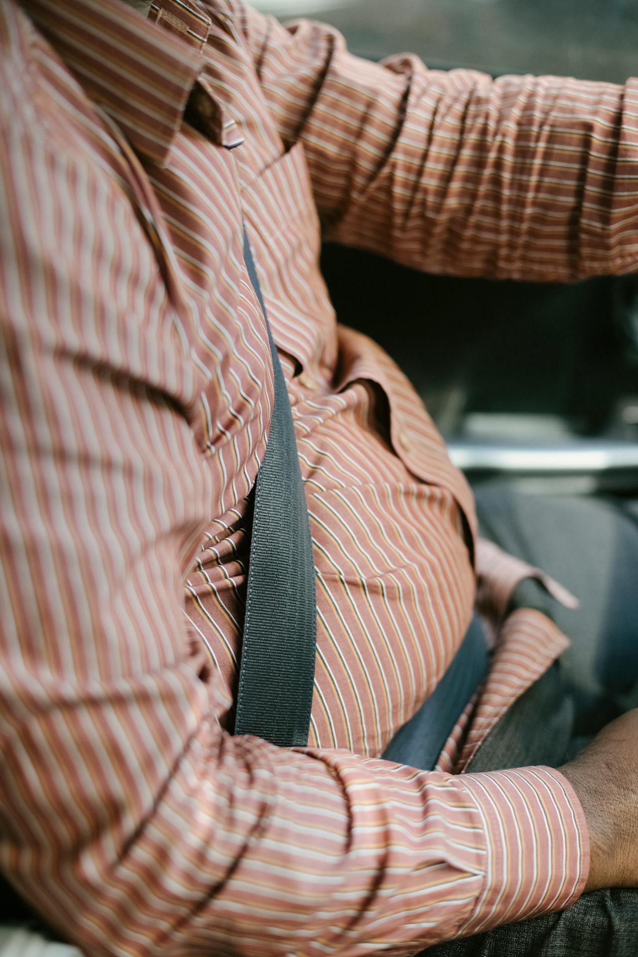 A man in a red striped shirt wears a fastened seatbelt on the driver's seat.